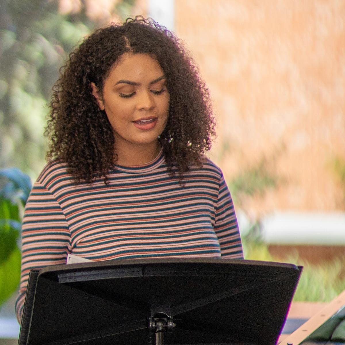 Caelia Marshall sings with sheet music on a music stand in a 教师 rehearsal space